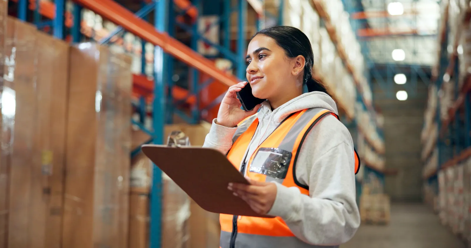 Purchasing manager on the phone holding a clipboard between warehouse racking
